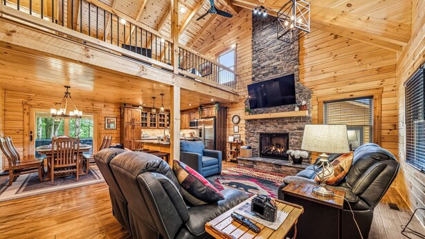 Un interior espacioso de cabaña de madera con comedor, sala de estar, chimenea y un balcón.