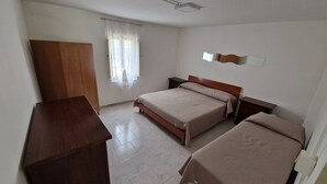 Ein Schlafzimmer mit zwei Betten, einem Holzschrank, einem Nachttisch, einer Deckenleuchte und einem Fenster mit durchsichtigem Vorhang.