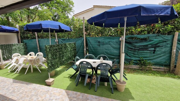 Eine Außenpatio mit grünem Kunstgrün, weißen Plastikstühlen und Tischen unter blauen Sonnenschirmen.