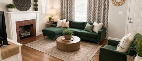 A living room with a fireplace, green sofa, round coffee table, and a ceiling fan.