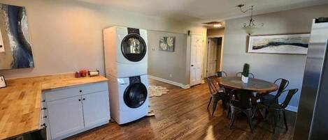 A compact kitchen with a dining area, wooden flooring, and a refrigerator.