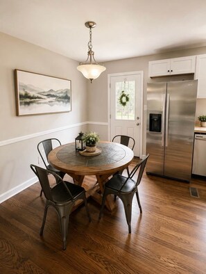 A dining area with a round table, four chairs, a chandelier, a refrigerator, and a door with a wreath. - Charming Home in Southland – Cozy & Spacious! (Lexington)
