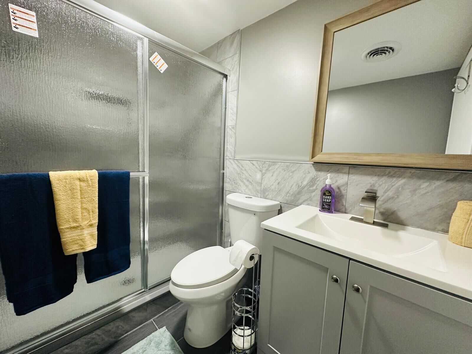 A bathroom with a glass shower door, a toilet, a sink with a mirror above it, and towels hanging on the wall.
