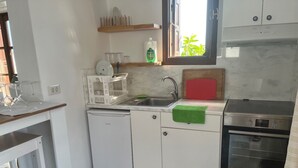 Eine kleine Küche mit weißen Schränken, einem eingebauten Geschirrspüler, einem Edelstahlbackofen und einem Fenster mit Blick auf Grünflächen.