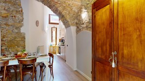 A dining area with a stone archway, wooden dining table, chairs, and a kitchen in the background.