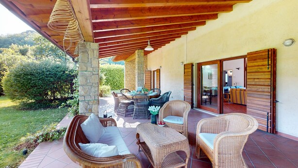 A covered patio with wicker furniture, stone pillars, and a view of the garden.