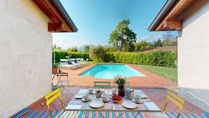 An outdoor dining area with a pool view, tables set with plates and cups, and yellow chairs.
