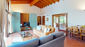 A spacious living room with a wooden ceiling, a sofa, a television, and a dining area with a table and chairs.