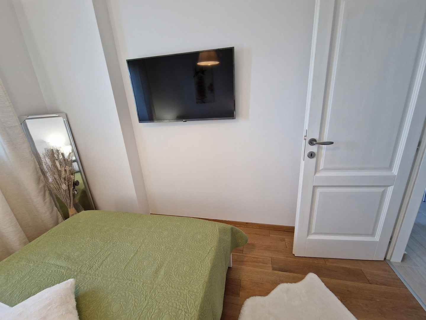 Ett sovrum med en säng, en tv som är monterad på väggen och en dörr.