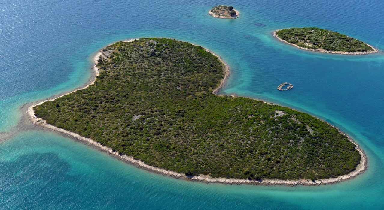 An aerial view of a heart-shaped island with clear turquoise waters and lush greenery.