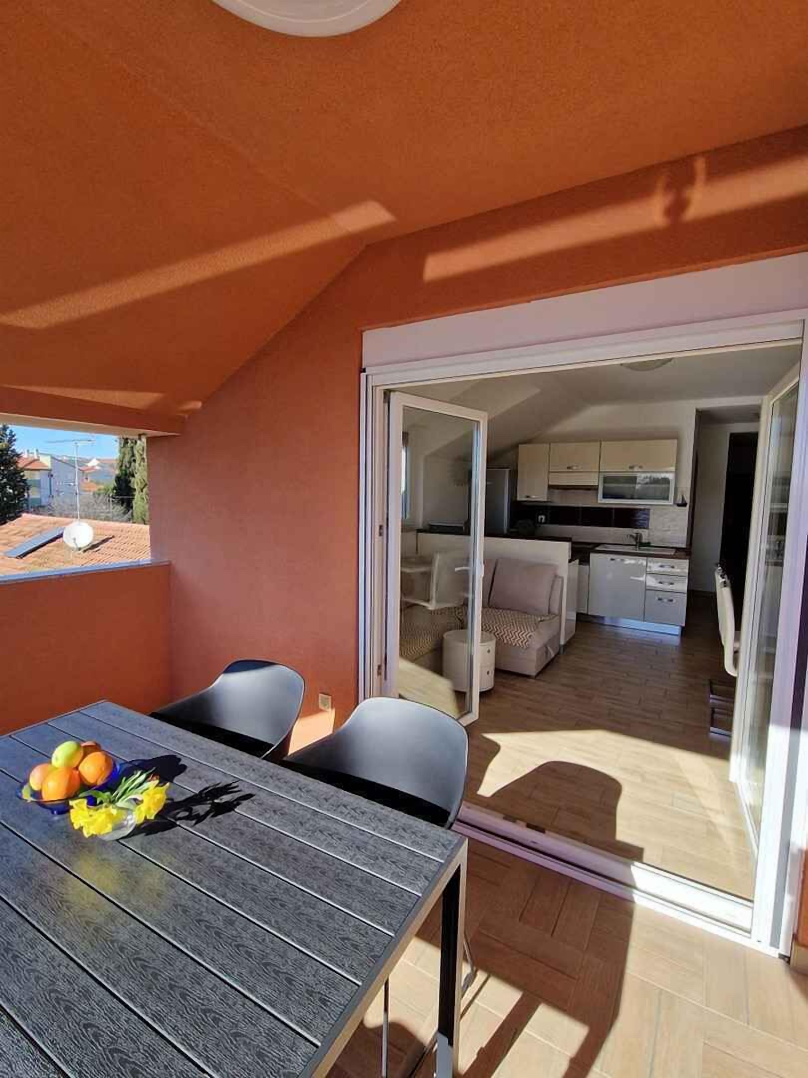 Un apartamento moderno con balcón, un área de comedor con mesa y sillas, y una cocina visible a través de un cristal.
