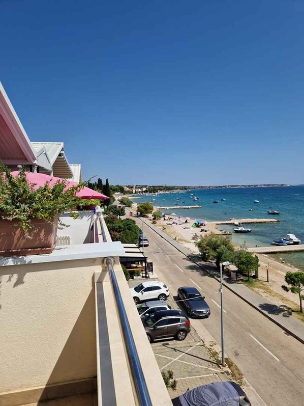 A balcony with a view of a beach, parked cars, and a clear blue sky.