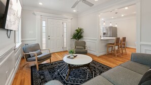 A living room with a ceiling fan, a TV mounted on the wall, a dining area with chairs, and a kitchen area with appliances. - NEW!! Cozy Arlington Home Near DC (Arlington)