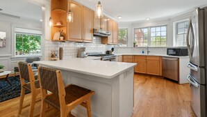 A modern kitchen with white cabinetry, a central island, wooden chairs, and a stainless steel refrigerator. - NEW!! Cozy Arlington Home Near DC (Arlington)