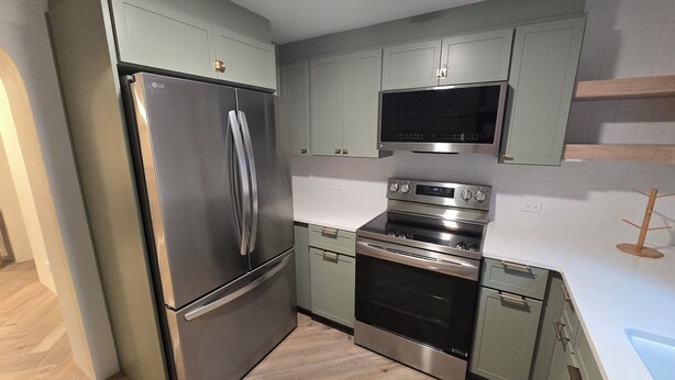 Une cuisine moderne dotée d’appareils électroménagers en acier inoxydable, de meubles de couleur vert clair et d’un parquet en bois disposé en motif chevrons.