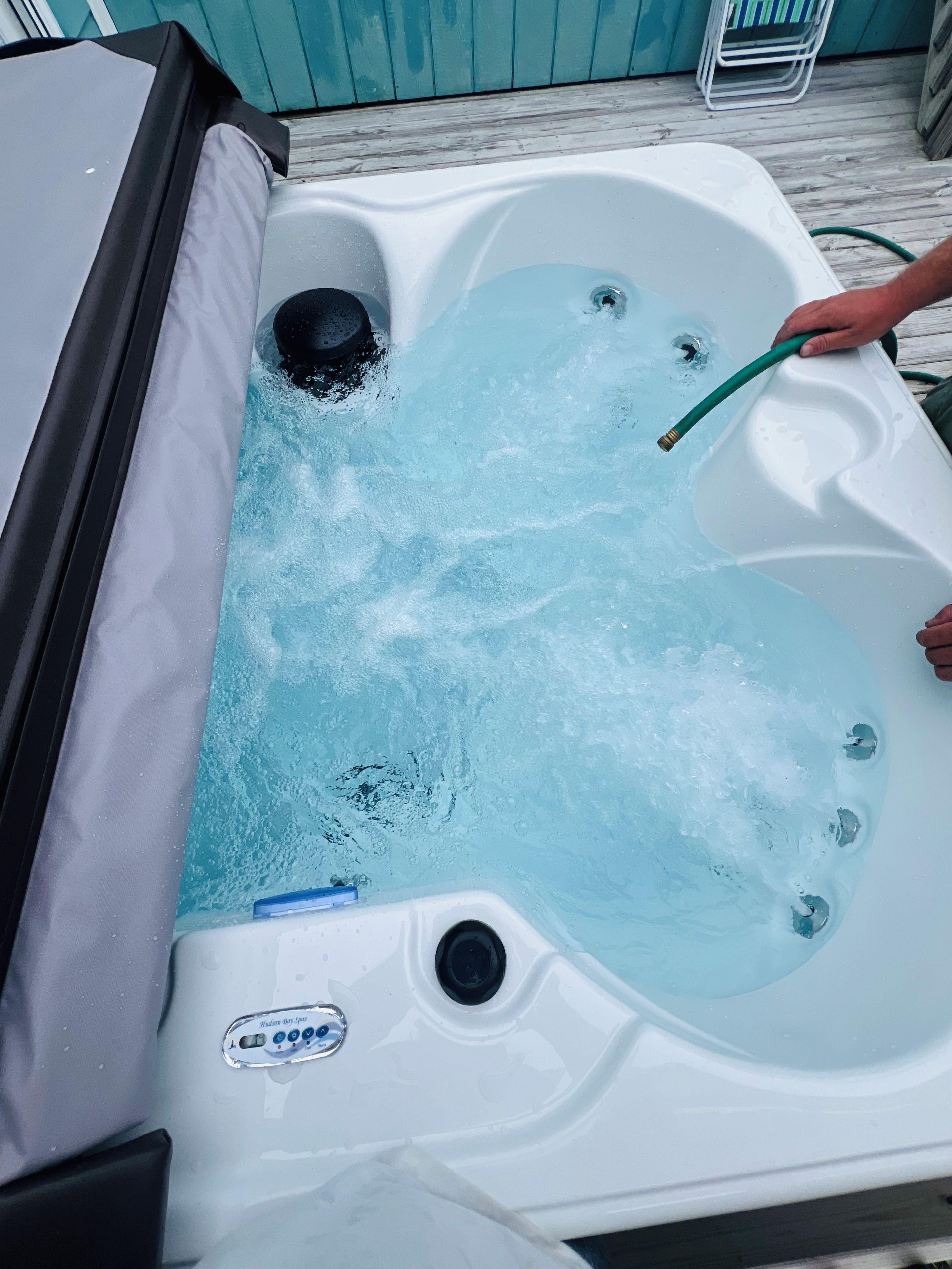 A hot tub with a person using a hose to fill it.