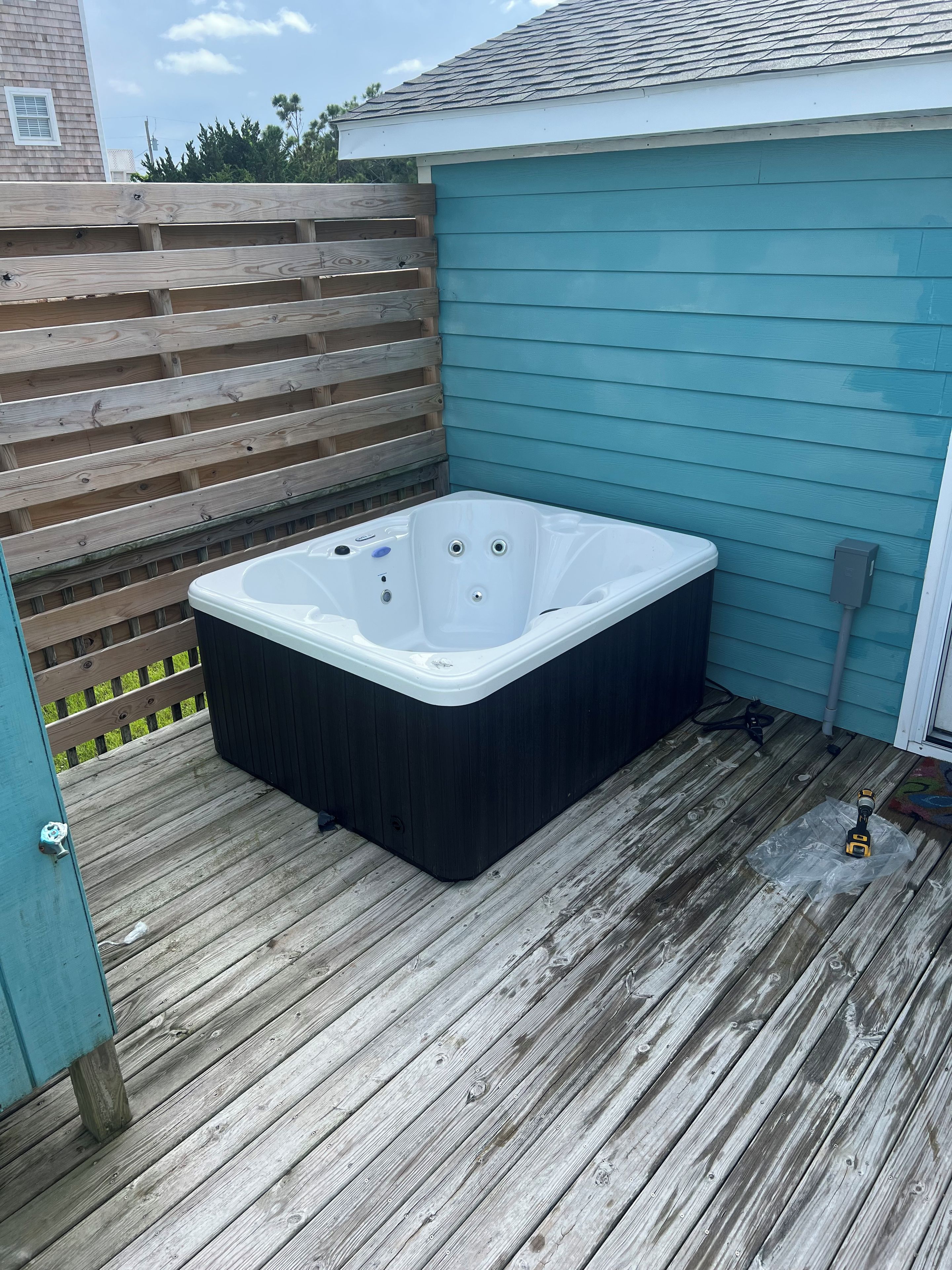 A hot tub on a wooden deck with a blue house in the background.