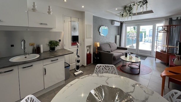 A modern kitchen with white cabinets, a marble countertop, and a sink. There is a dining area with a round table and chairs, a sofa, and a TV stand. - Port-Fréjus, 400m from the beaches, cozy 28m2 studio, air conditioning, terrace, private parking, ideal for 2 people (Fréjus)