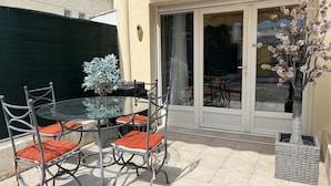 A patio with a glass table and metal chairs, a small tree, and a sliding glass door. - Port-Fréjus, 400m from the beaches, cozy 28m2 studio, air conditioning, terrace, private parking, ideal for 2 people (Fréjus)