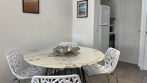 A dining area with a round marble table, white chairs, and two framed pictures on the wall. - Port-Fréjus, 400m from the beaches, cozy 28m2 studio, air conditioning, terrace, private parking, ideal for 2 people (Fréjus)
