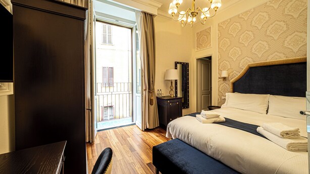 Une chambre d’hôtel avec un grand lit, un bureau, une chaise, une commode, un miroir, une table de chevet et un lustre.