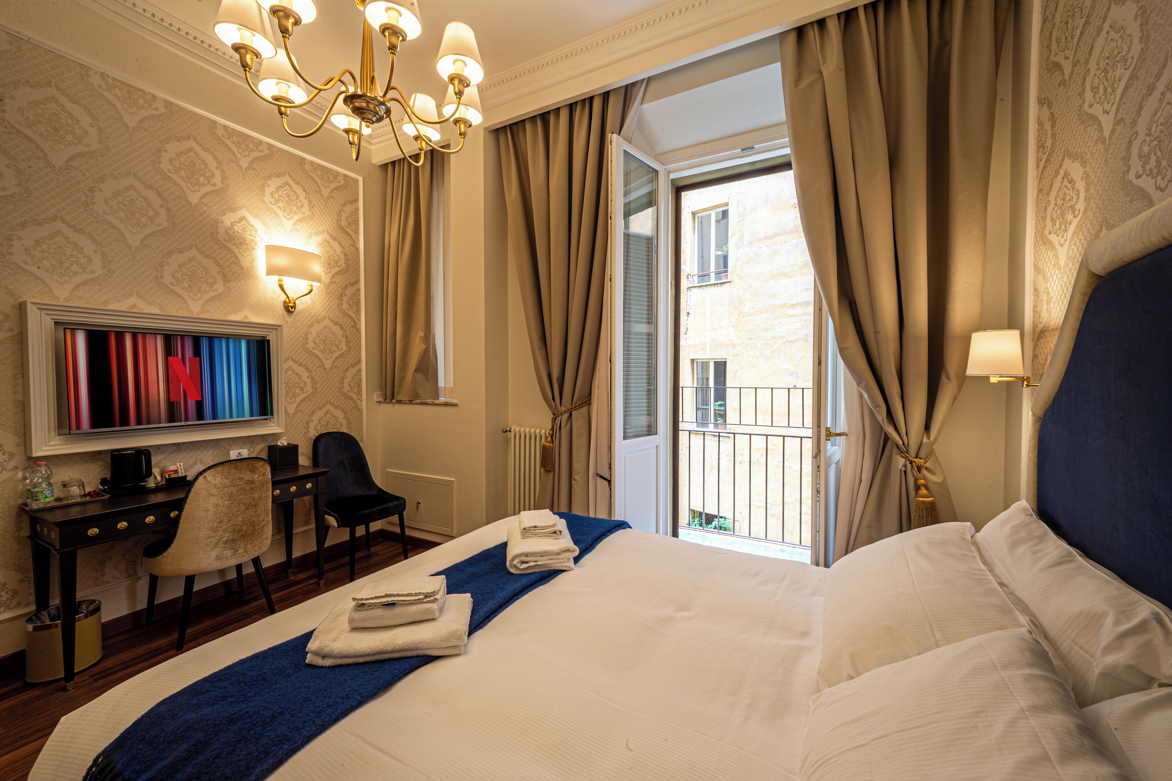 A hotel room with a large bed, a desk with a chair, a television, and a view of the outside balcony.