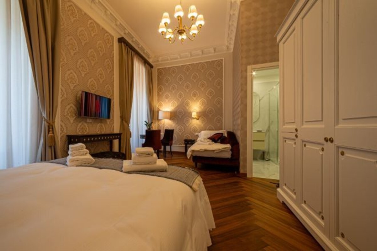 A hotel room with a large bed, a desk, a chair, and a wardrobe.