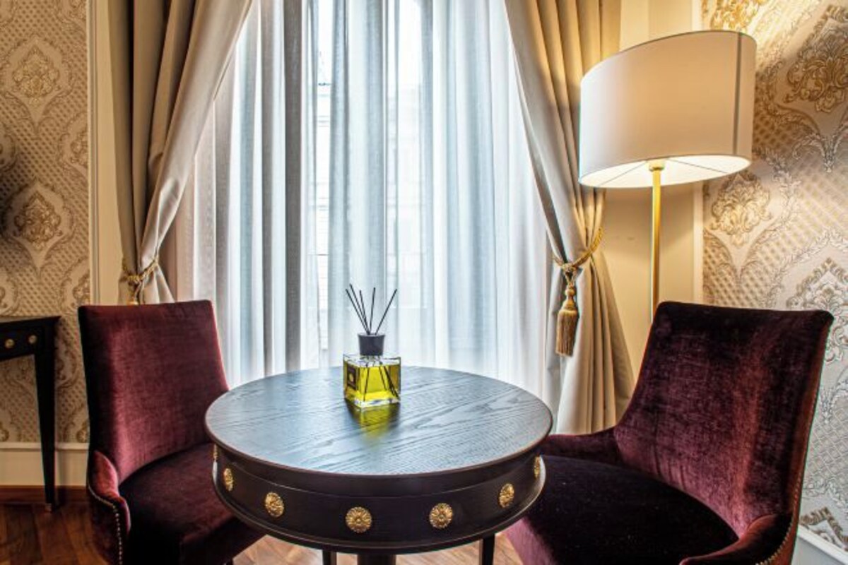 A room with a round table, two chairs, a lamp, and a window with curtains.