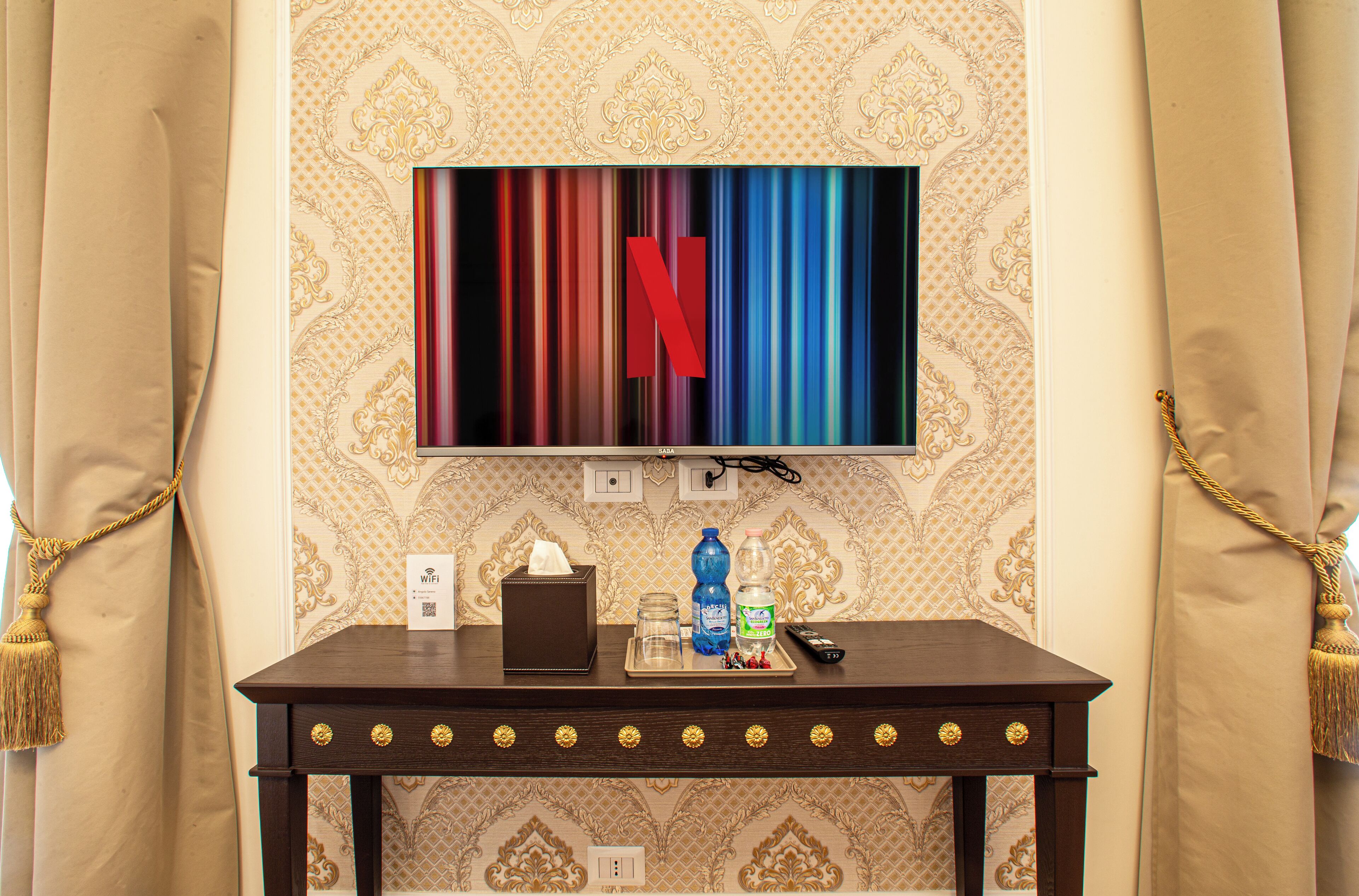 Et hotelværelse med et fjernsyn, der viser Netflix-logoet, et lille bord med en servietæller, en vandflaske, et glas og en fjernbetjening.