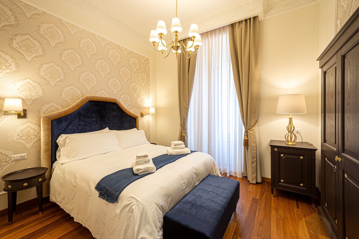 A hotel room with a large bed, a bedside table, a lamp, and a wardrobe.
