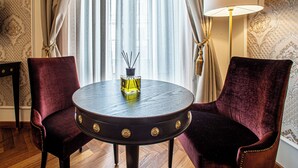 Une pièce avec une table ronde, deux chaises, une lampe et une fenêtre avec des rideaux.
