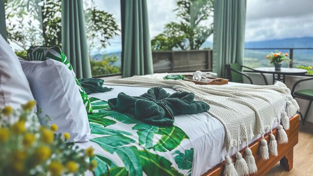 A bedroom with a large bed, a view of the outdoors, and a balcony with a table and chairs. -  Volcano and Lake View, Eco Glam #1. (La Fortuna)