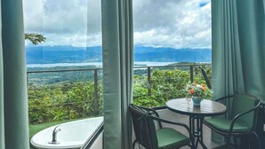 A balcony with a view of a mountainous landscape, a round table with chairs, and a bathtub. -  Volcano and Lake View, Eco Glam #1. (La Fortuna)