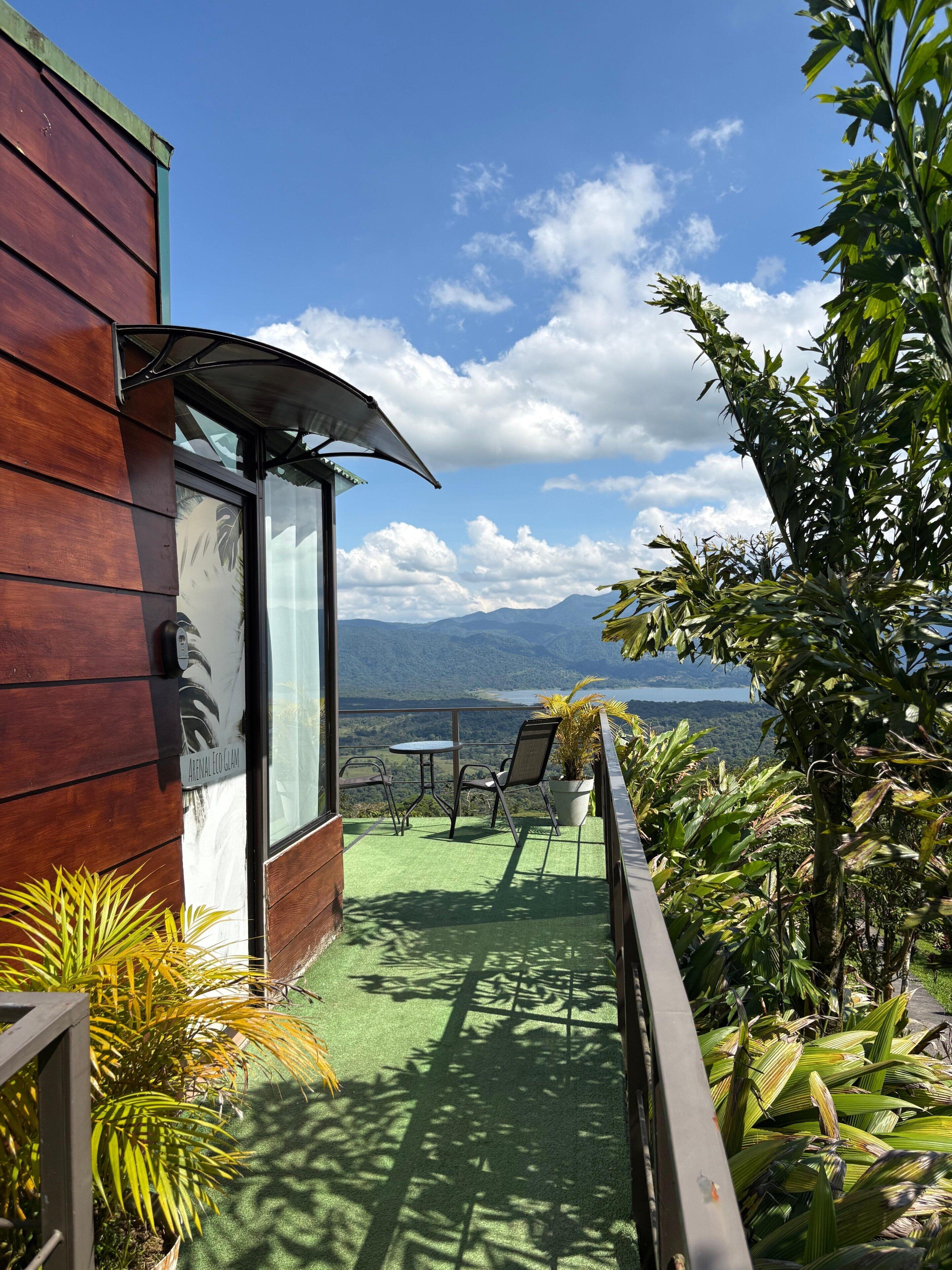 Uma varanda com vista para montanhas e um lago, um edifício de madeira e plantas em vasos.
