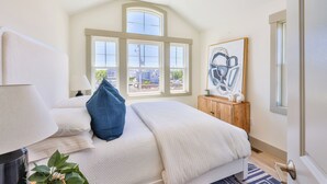 Une chambre à coucher avec un grand lit, une fenêtre à carreaux, une armoire en bois et une œuvre d’art encadrée accrochée au mur.