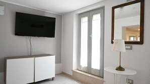 Une pièce dotée d’un téléviseur à écran plat, d’une armoire blanche, d’une petite table avec une lampe et d’une fenêtre avec des rideaux.
