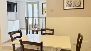 Un coin repas avec une table blanche et quatre chaises en bois, un téléviseur fixé au mur et un tableau encadré au-dessus de la table.