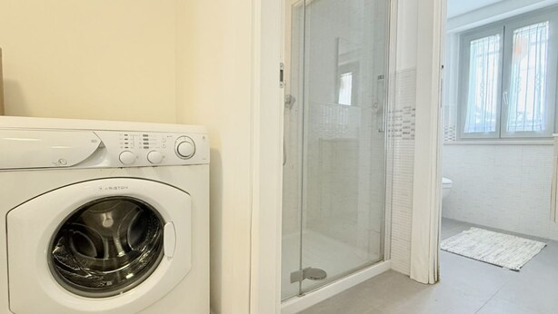 Un espace buanderie équipé d’un lave-linge, d’une douche à parois de verre et offrant une vue sur la salle de bain.
