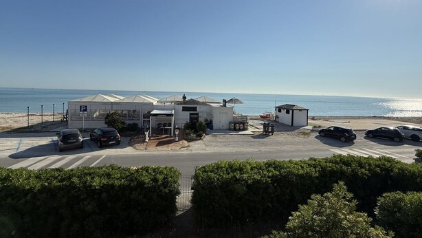 Un hotel frente al mar con estacionamiento, vistas a la playa y una pequeña construcción contigua.