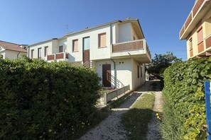 Ein zweigeschossiges Wohngebäude mit Balkon, Kiesweg und dichter Bepflanzung.
