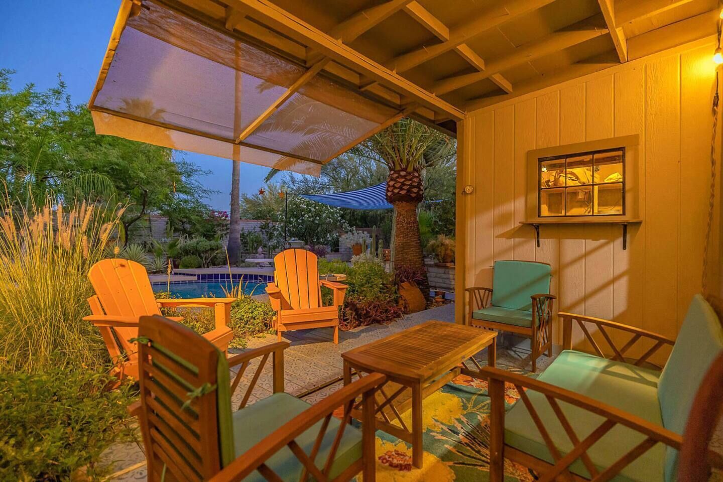 Une terrasse extérieure avec des chaises et une table en bois, une piscine et un espace couvert offrant une vue sur la piscine et le jardin.
