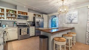 A modern kitchen with white cabinetry, stainless steel appliances, a central island with stools, and a decorative chandelier. - Poolside Oasis, Luscious Gardens, and Spacious 4-bedroom house in Tucson (Tucson)