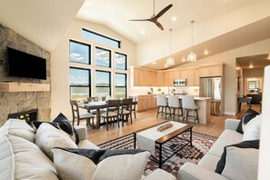 A spacious living area with a large sofa, a coffee table, and a fireplace. There is a dining area with a table and chairs, and a kitchen with modern appliances.