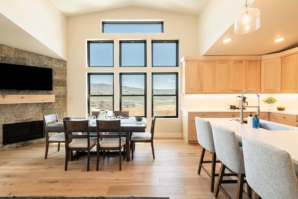 A modern kitchen with a stone fireplace, large windows, and a dining area with a table and chairs.
