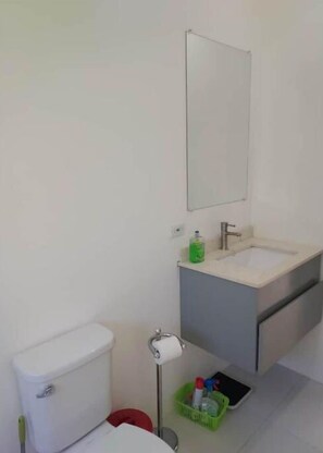 A bathroom with a white toilet, a sink with a mirror above it, and a green basket on the floor. - Relax and Reconnect: A peaceful holiday home nestled in lush green surroundings. (Upton,  Ocho Rios)