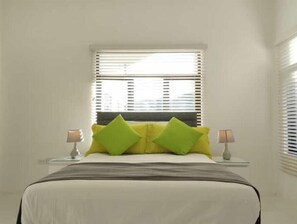 A neatly made bed with a gray bedspread and two green pillows, flanked by bedside tables with lamps. - Relax and Reconnect: A peaceful holiday home nestled in lush green surroundings. (Upton,  Ocho Rios)