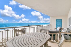 Ein Balkon mit Holztisch und -stühlen, einer blauen Tür und Blick auf Strand und Meer.