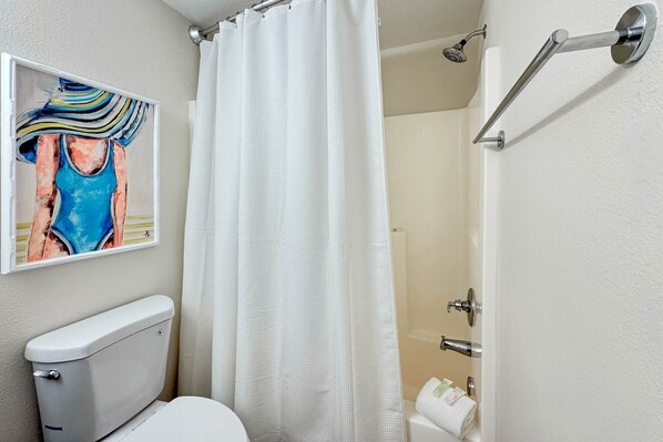 A bathroom with a white toilet, a shower with a white curtain, and a painting of a swimsuit on the wall.
