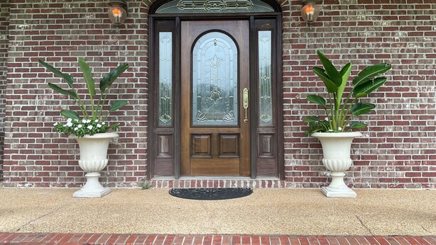 A brick building with a dark wooden door, two potted plants, and a doormat.