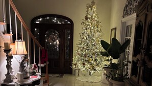 A warmly lit living room with a Christmas tree, a staircase, and a dining area.
